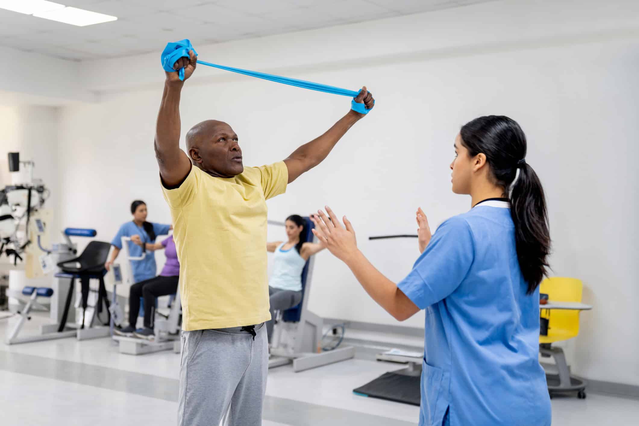 Senior man performing shoulder impingement exercises with resistance band guided by physical therapist